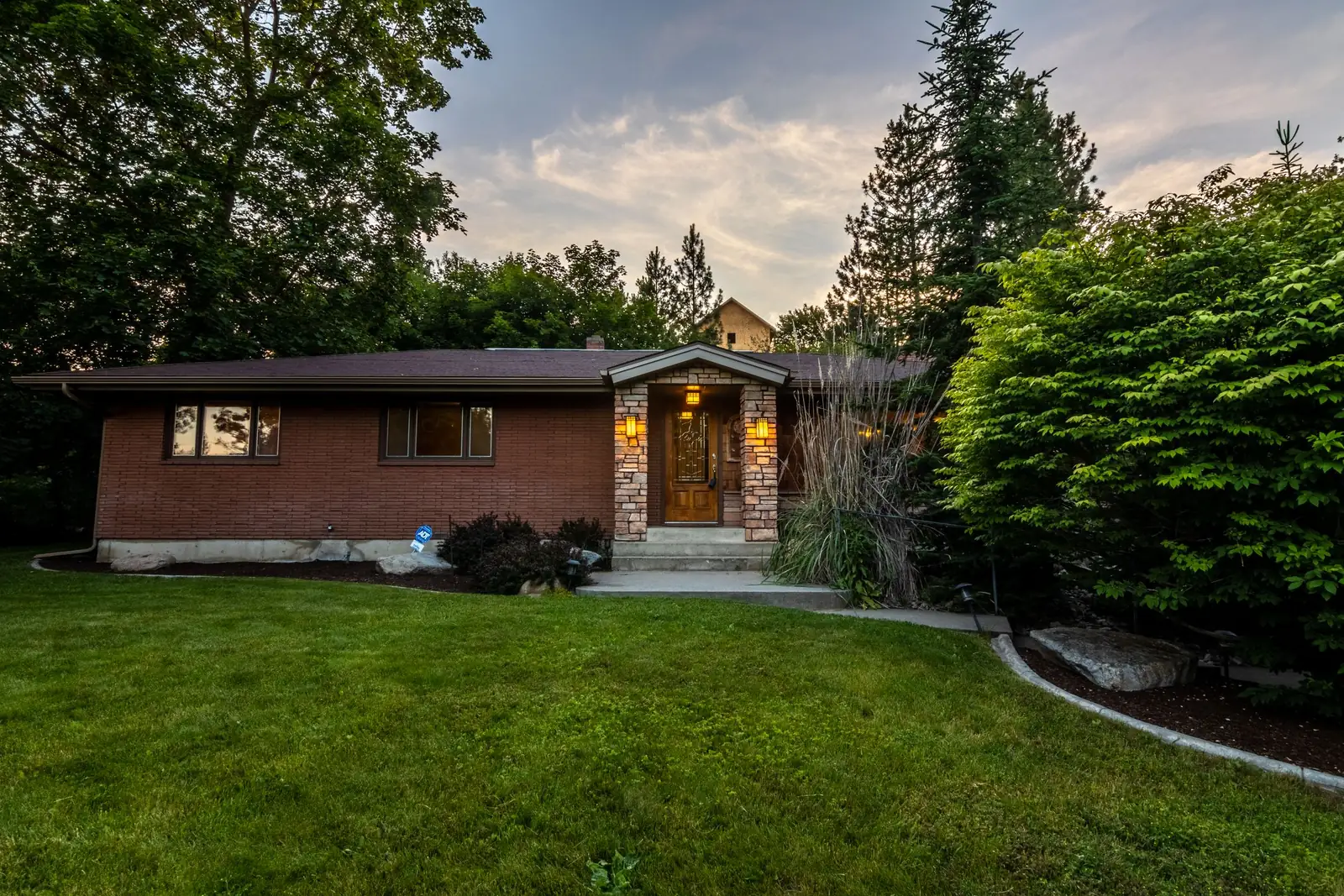 Brick home with a lawn and trees at dusk